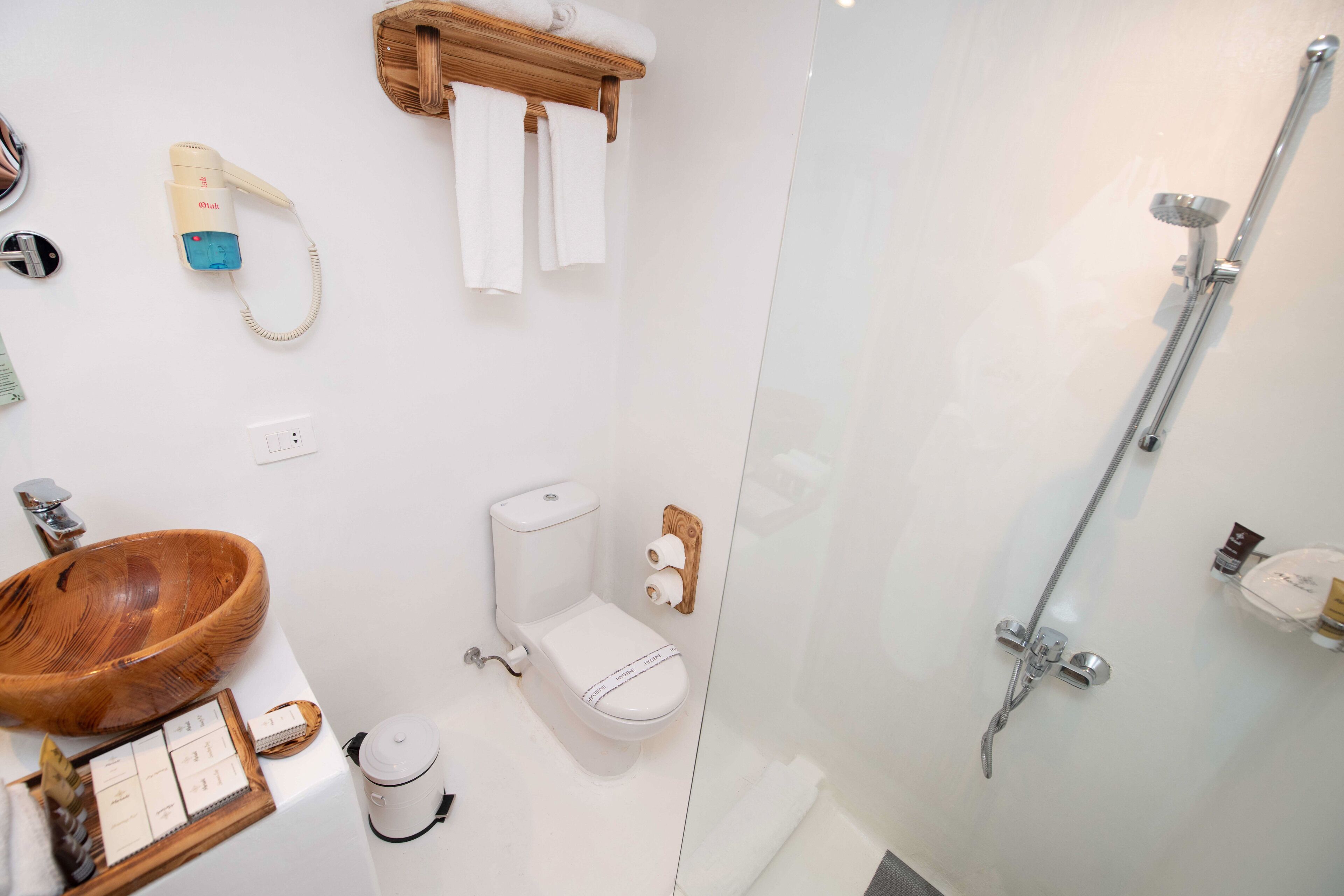 A modern bathroom with a wooden bowl sink, a toilet, a shower, and a hairdryer on the wall.