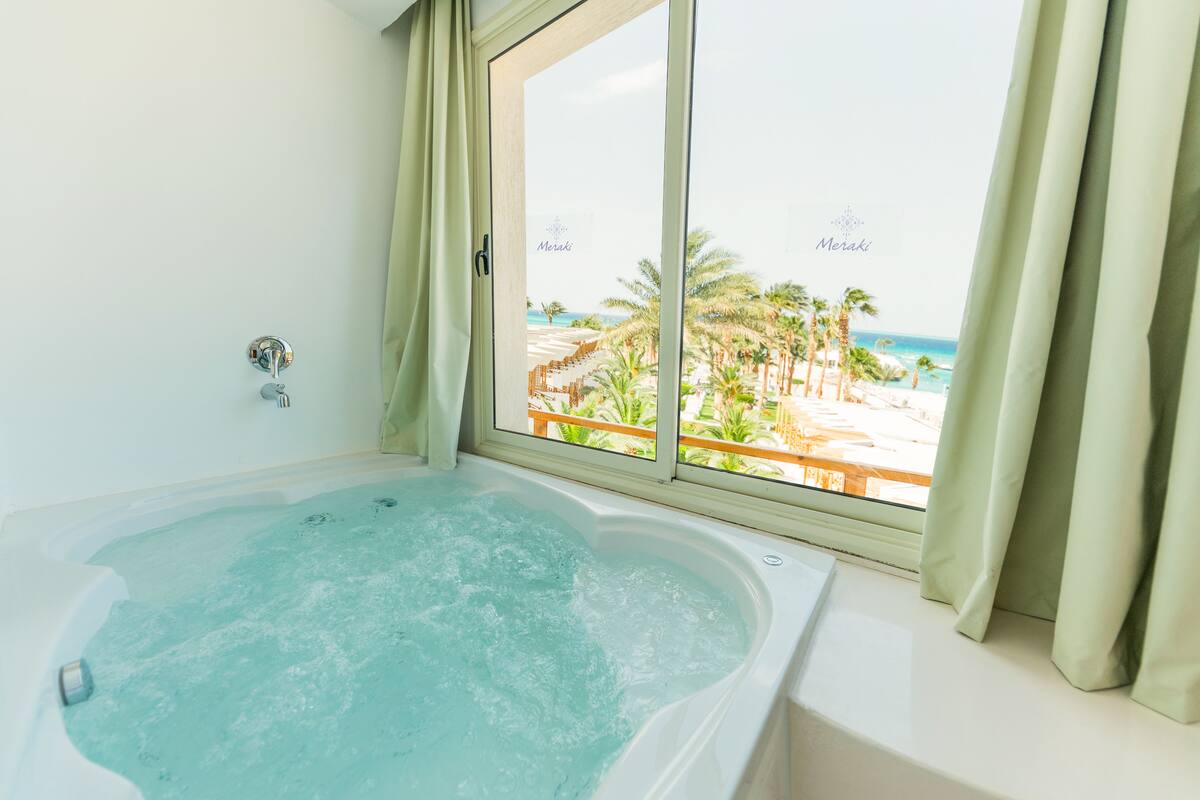 Ein Badezimmer mit einer großen Badewanne und einem Fenster mit Blick auf einen Strand.
