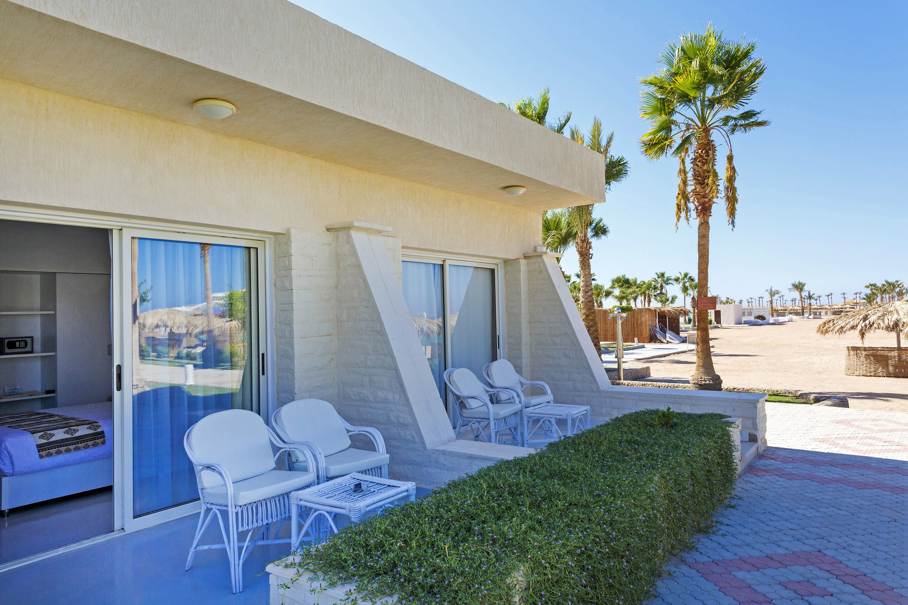 A modern hotel room with a sliding glass door, white wicker furniture, and a view of the beach.