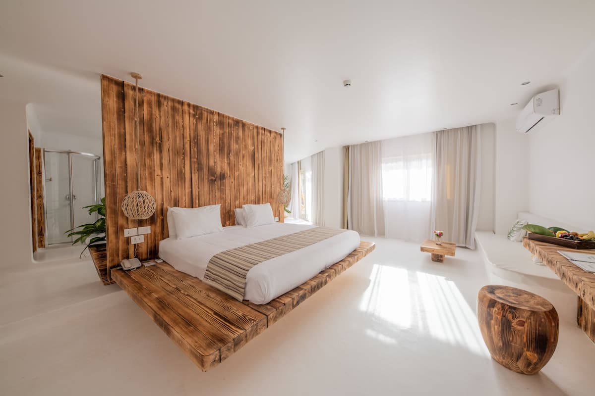 Ein modernes Schlafzimmer mit einem Holzkopfteil, einem großen Bett, Nachttischen, einem kleinen Beistelltisch und einem hölzernen Hocker.