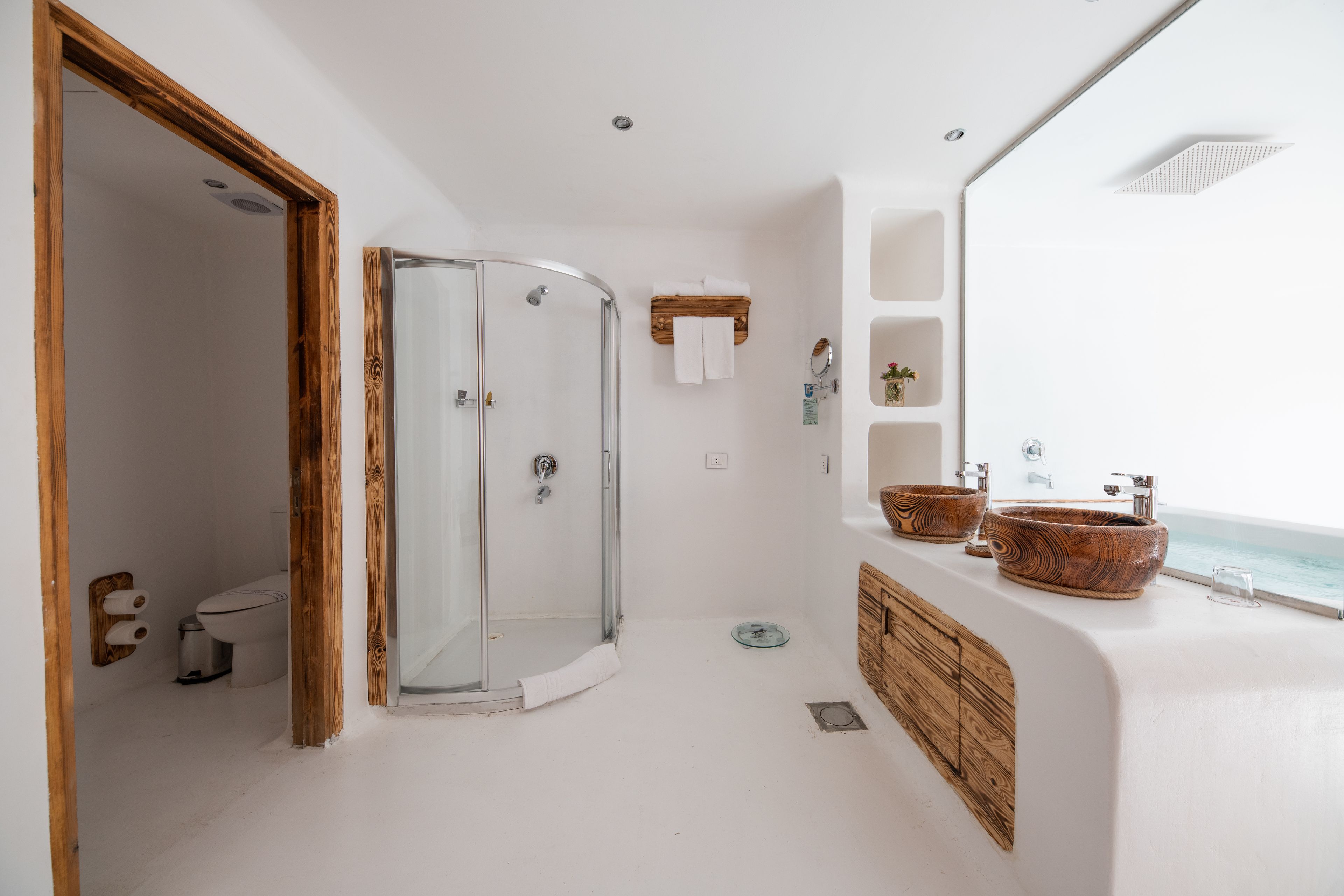 A modern bathroom with a glass shower, wooden accents, and a view of the ocean.