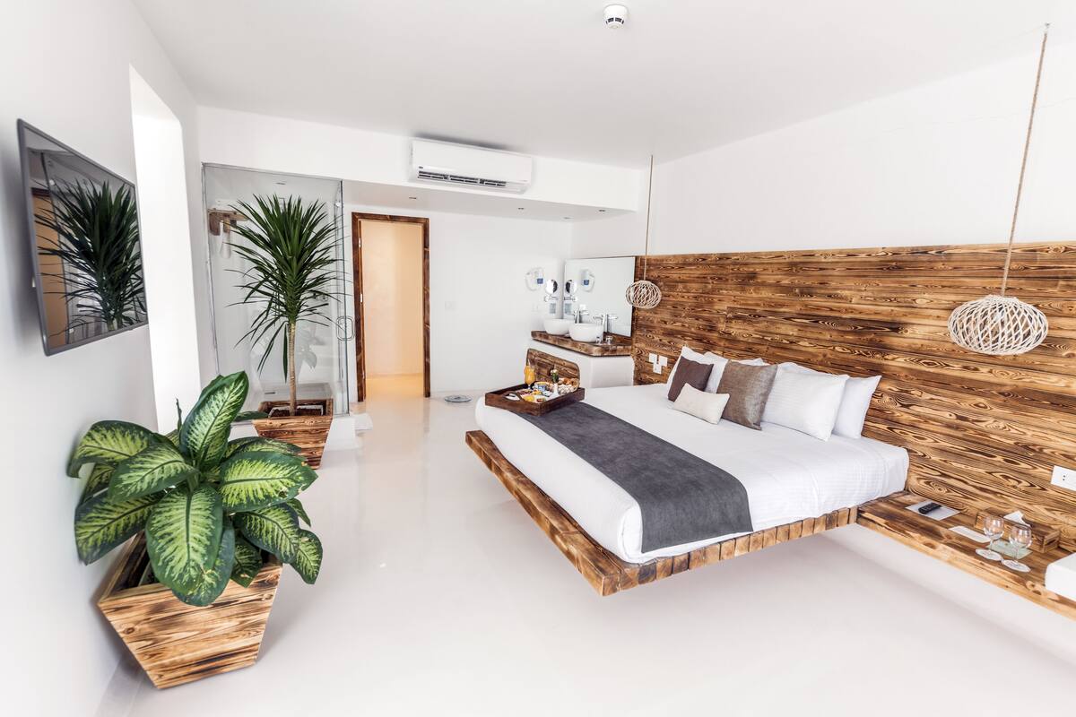 Ein modernes Schlafzimmer mit einem Holzkopfteil, einem großen Bett, einem Nachttisch mit Tablett und einer Zimmerpflanze.