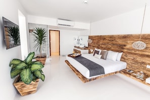 A modern bedroom with a wooden headboard, a large bed, a bedside table with a tray, and a potted plant.