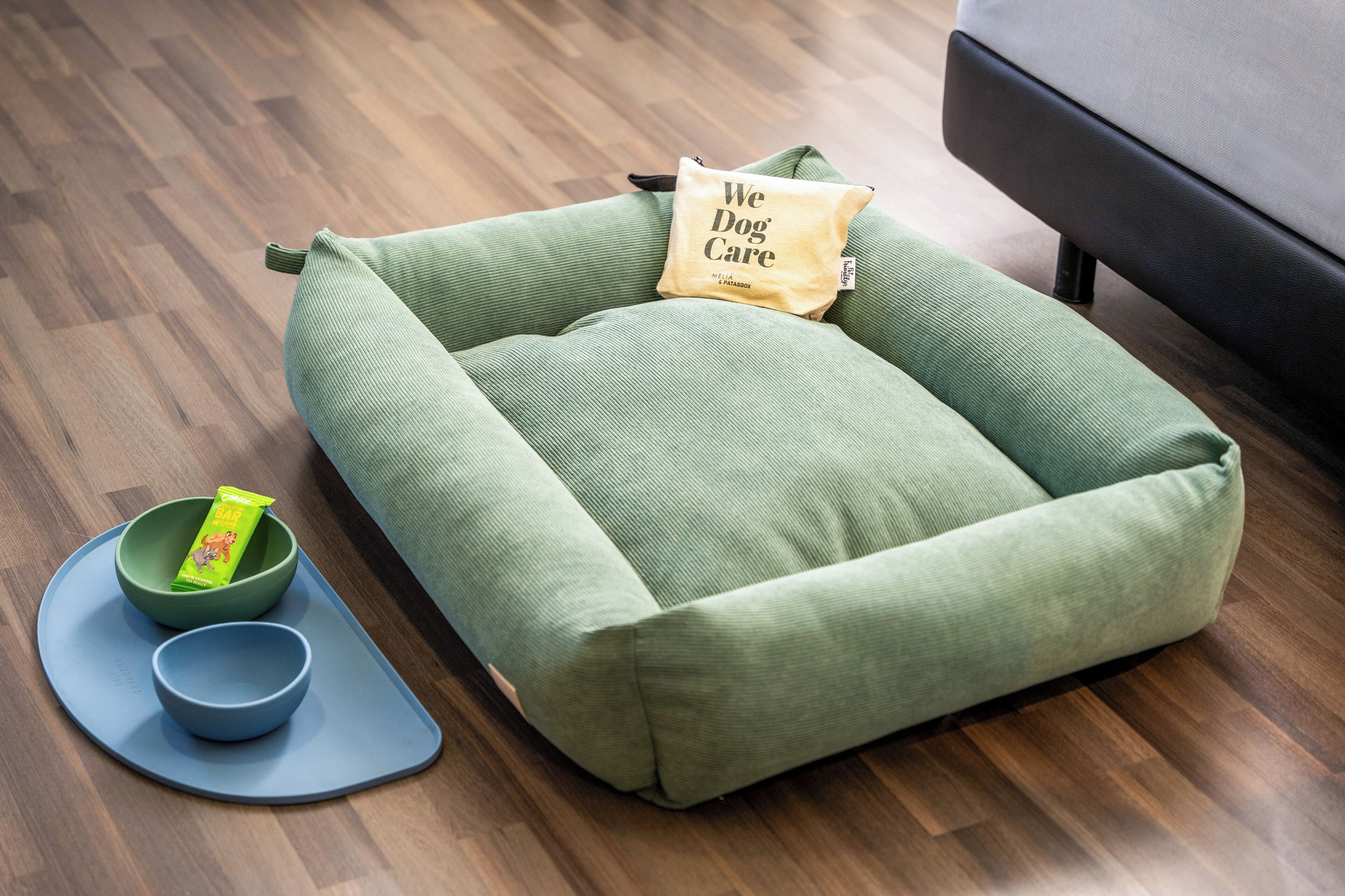 A pet bed with a pillow, a bowl, and a mat on a wooden floor.