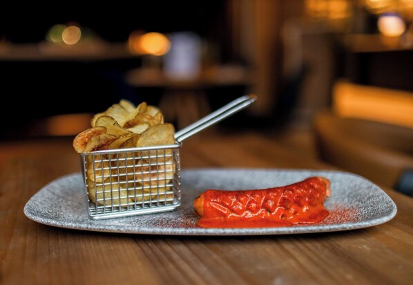 A plate with a small wire basket containing chips and a red sauce-covered item, possibly a sausage, on a textured plate. - INNSiDE by Meliá Berlin Mitte (Berlin)