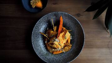 A dark wooden table with a textured bowl containing a dish with vegetables and a carrot.