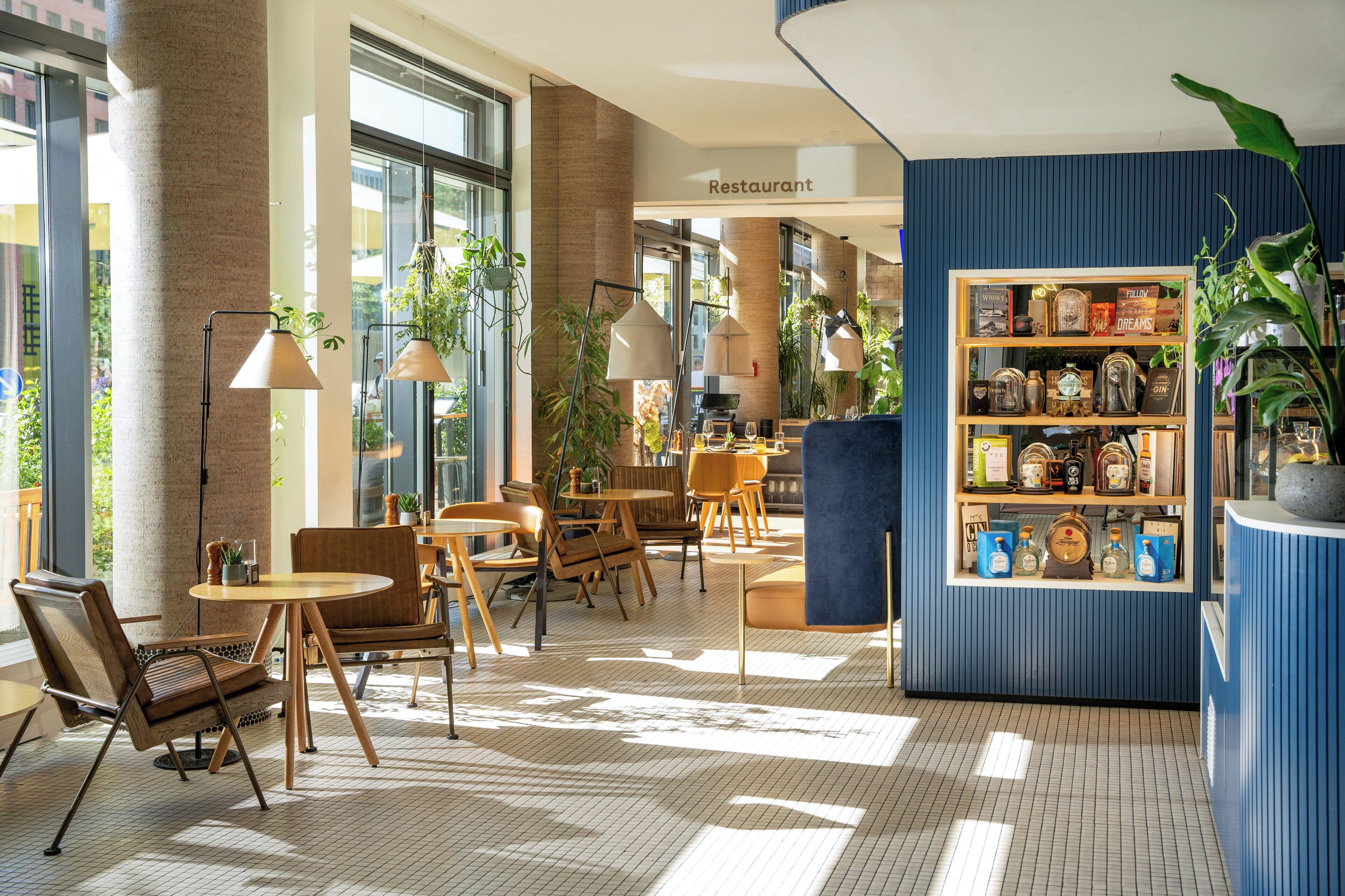 A modern restaurant interior with a mix of seating options, including round tables and chairs, and a display of bottles and glasses on shelves.