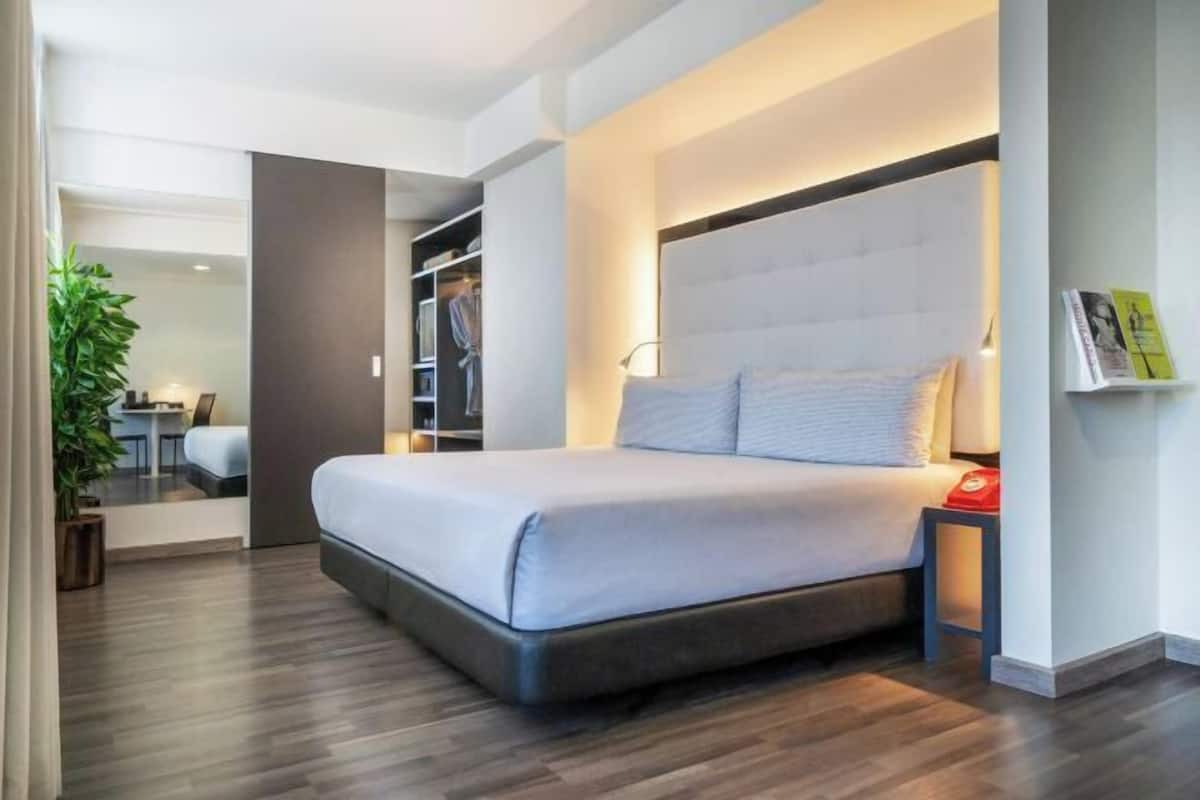 Habitación de hotel moderna con una cama grande, una mesita de noche, un armario y un pequeño escritorio con una silla.