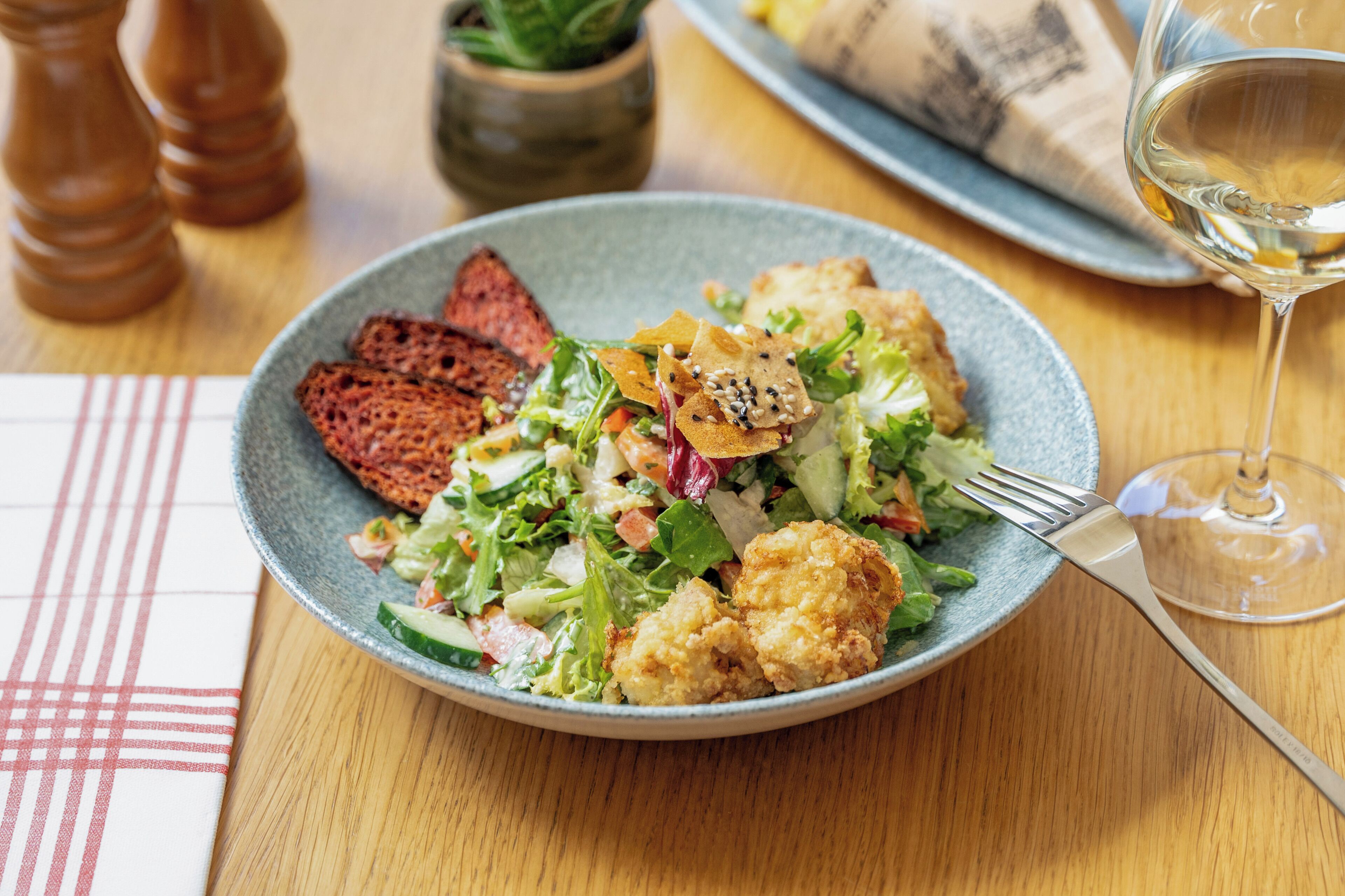 A plate of food with a salad, bread, and a glass of white wine on a wooden table.
