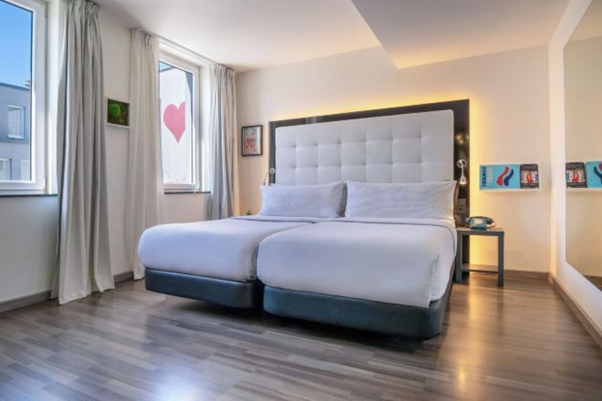 Une chambre à coucher moderne avec un grand lit, une table de chevet, une commode et une fenêtre avec des rideaux.