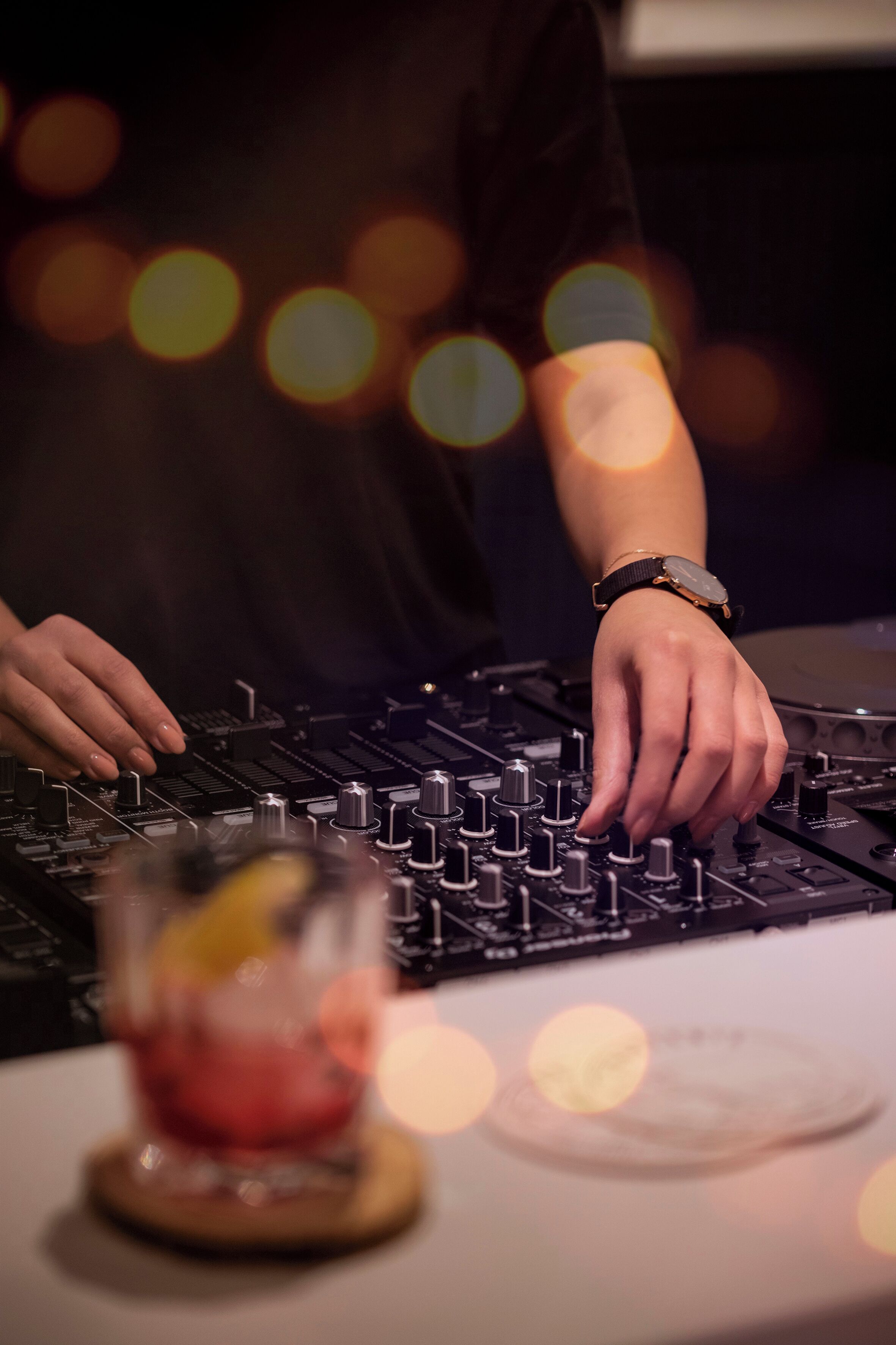 A person operating DJ equipment with a drink on a coaster.