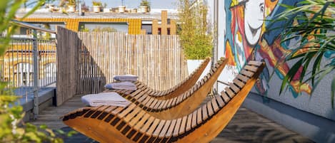 A wooden hammock chair on a wooden deck with a view of a building with a colorful mural.