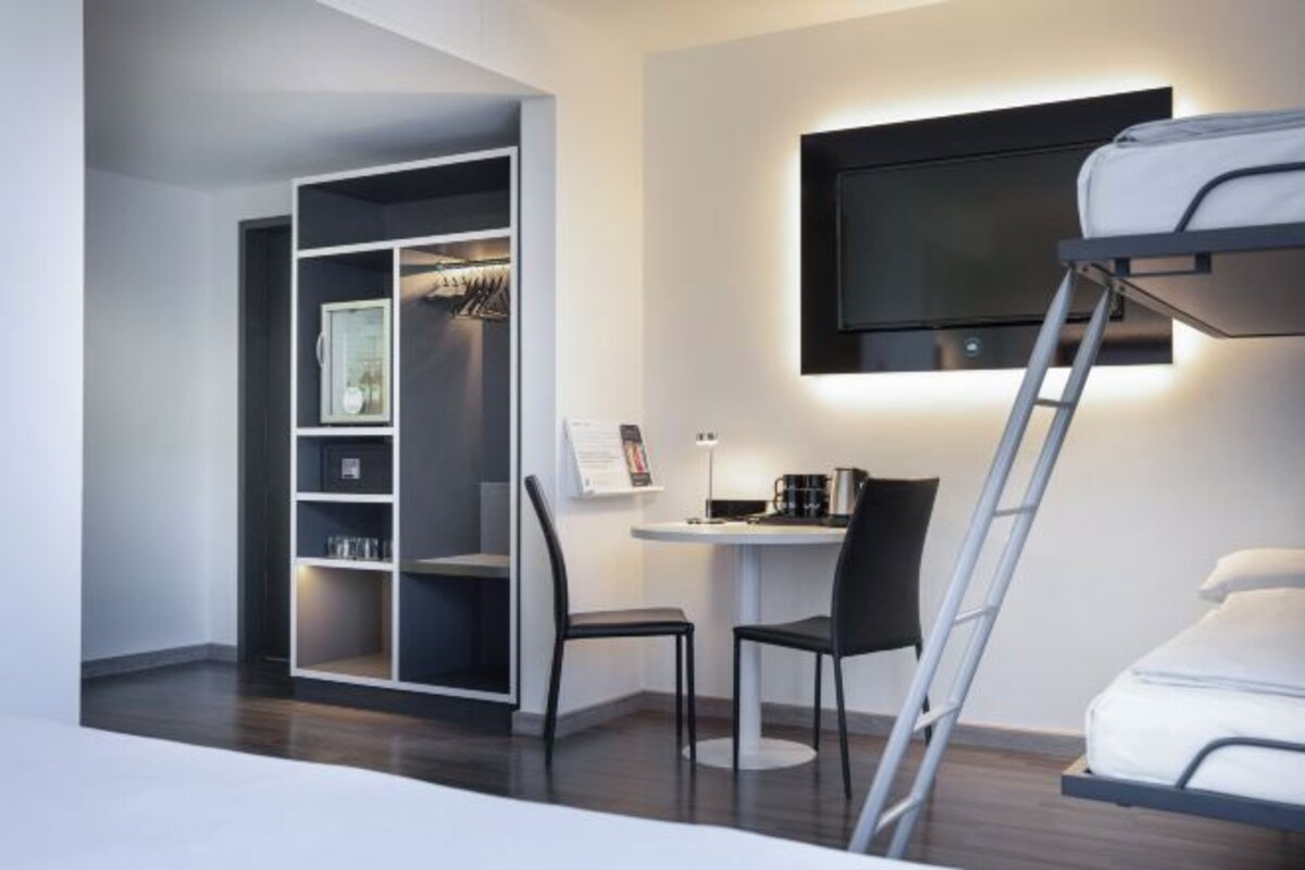 Une chambre moderne équipée d’un lit superposé, d’un bureau avec une chaise, d’une armoire et d’un téléviseur fixé au mur.