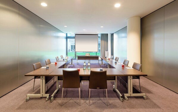 Ein Konferenzraum mit einem langen Tisch, Stühlen und einer Projektionsleinwand.