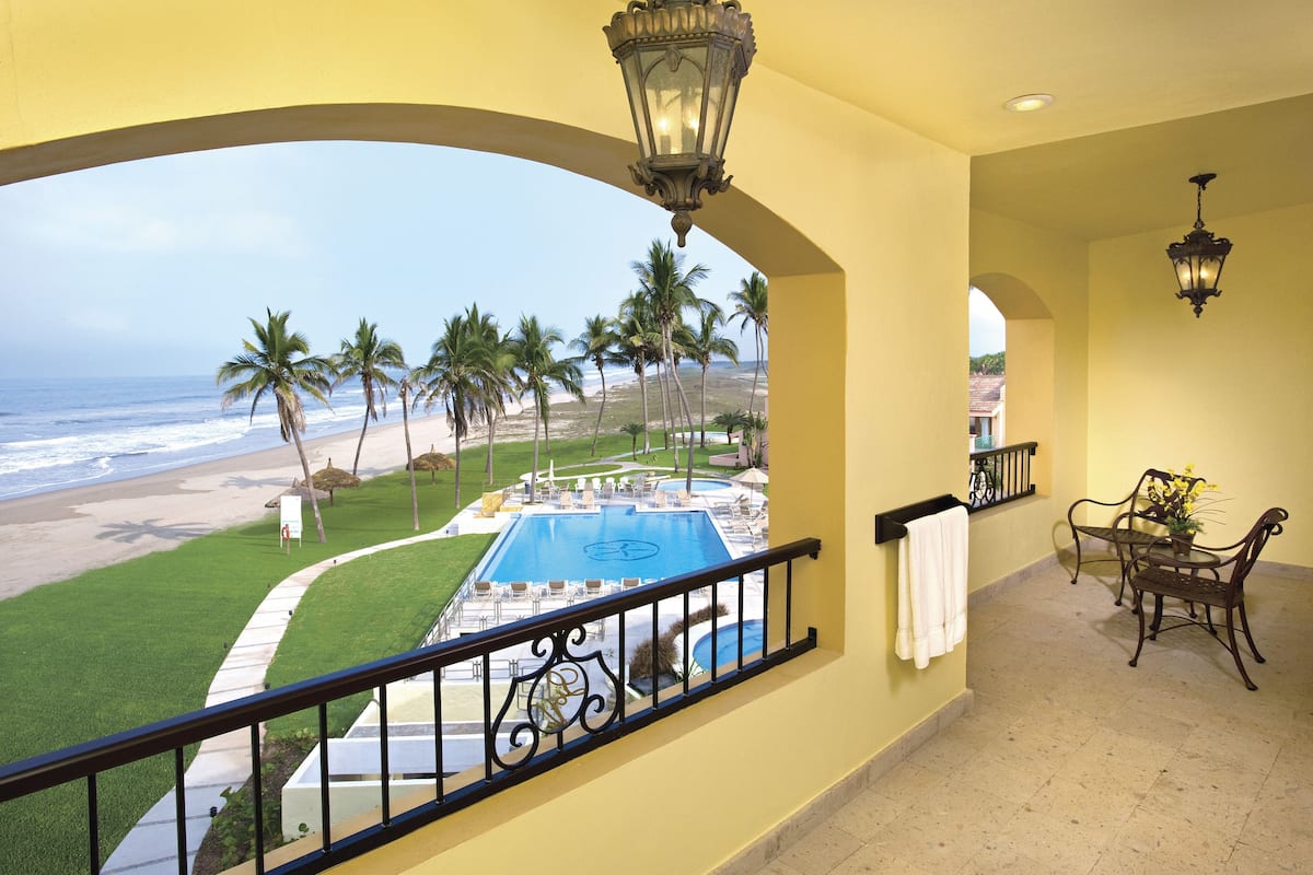 A balcony with a pool, palm trees, and a view of the beach.