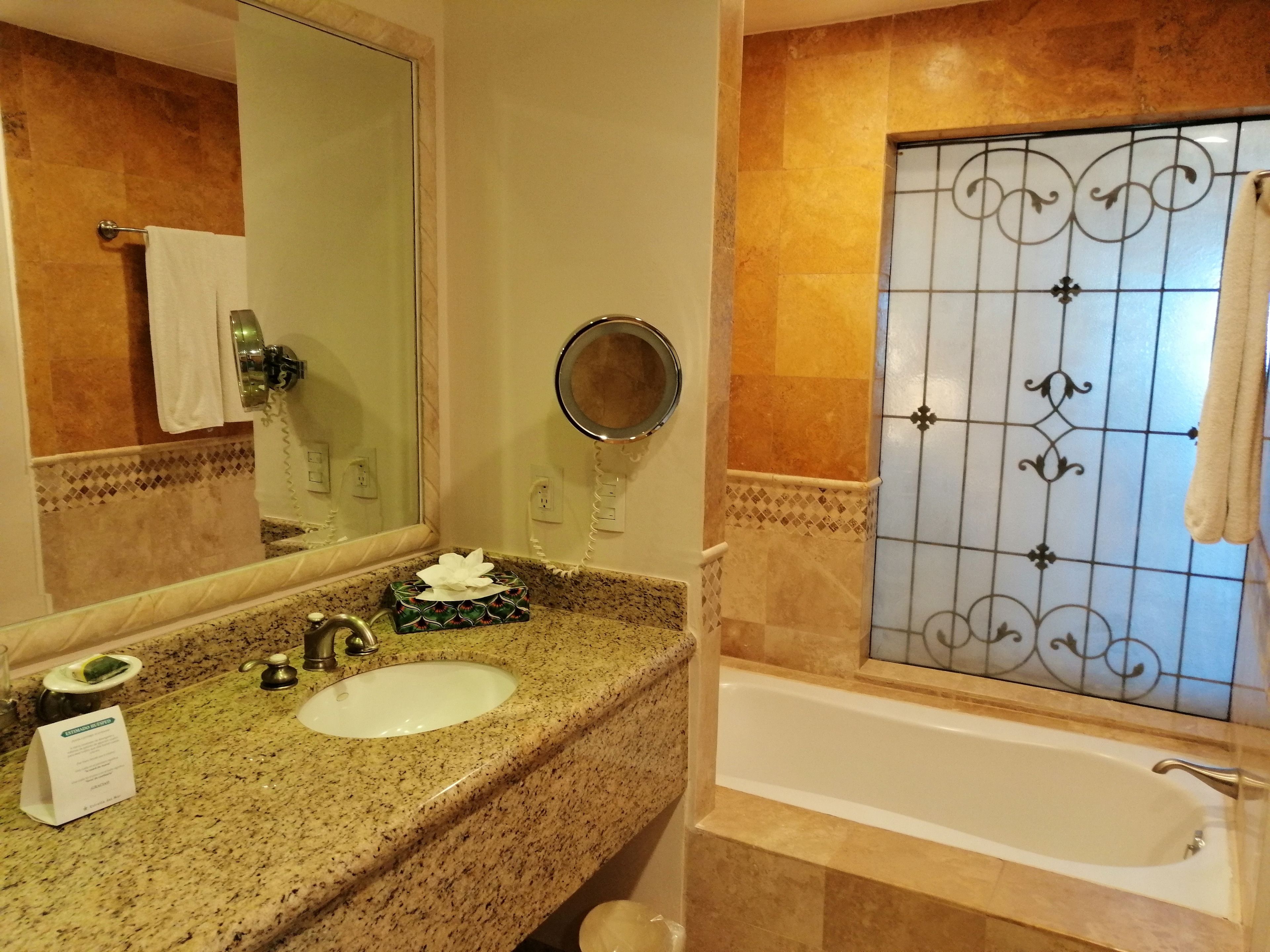 Un baño con encimera de granito, lavamanos, espejo, toallero y bañera.