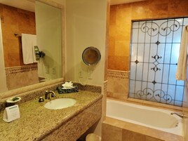 Un baño con encimera de granito, lavamanos, espejo, toallero y bañera.