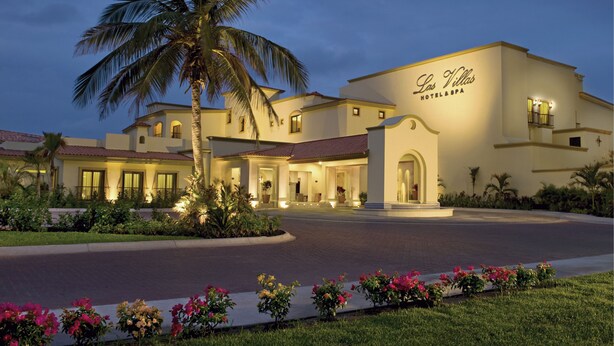 A hotel with a well-lit entrance, palm trees, and a clear sky. - Las Villas Hotel & Golf by Estrella del Mar (Mazatlán)