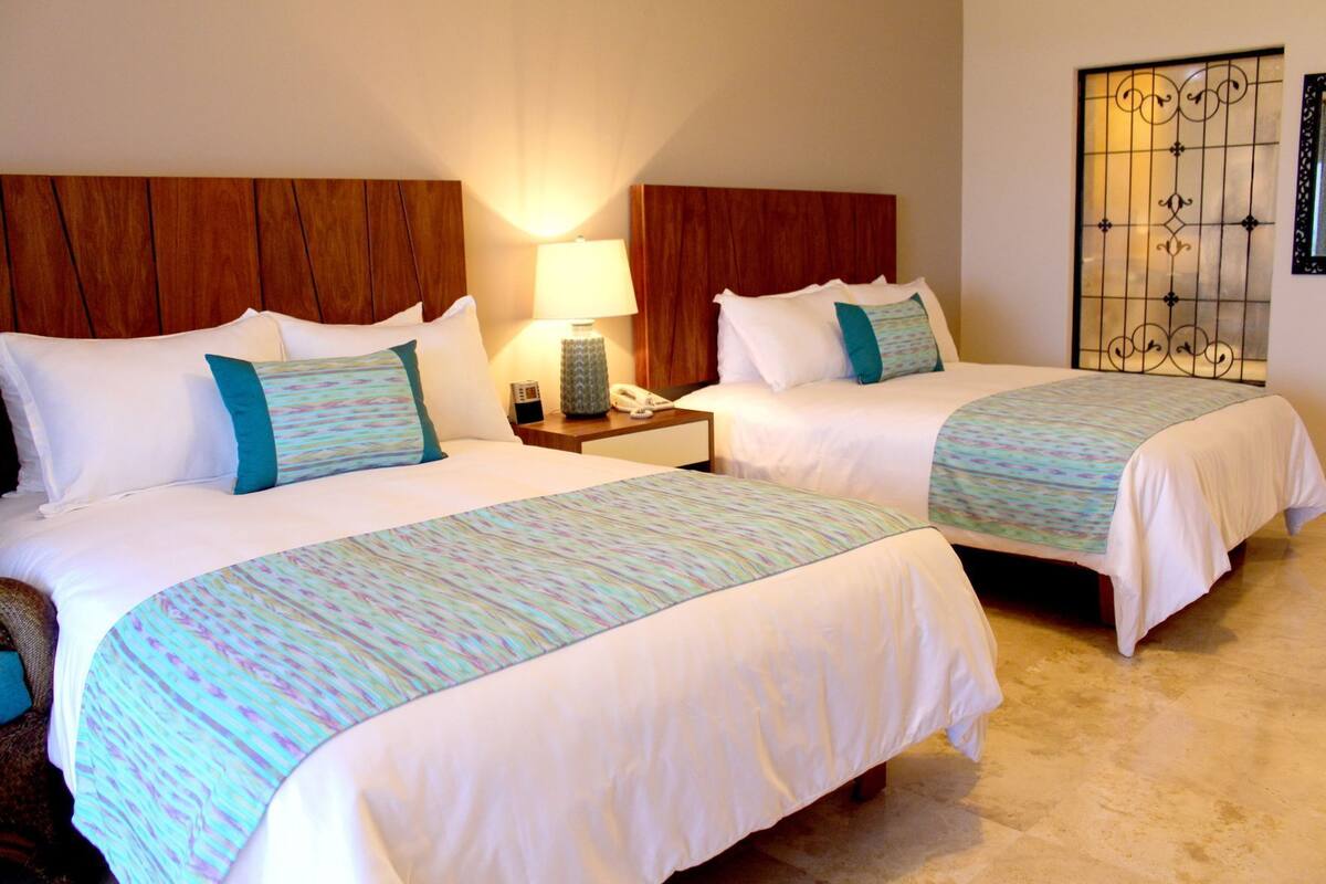 A hotel room with two beds, wooden headboards, a bedside lamp, a telephone, and a decorative metal screen.