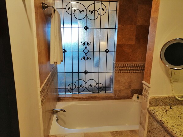Un baño con bañera, puerta de vidrio con barras de metal decorativas y tocador con espejo redondo.