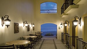 A corridor with tables and chairs, a view of the ocean, and decorative wall sconces. - Las Villas Hotel & Golf by Estrella del Mar (Mazatlán)