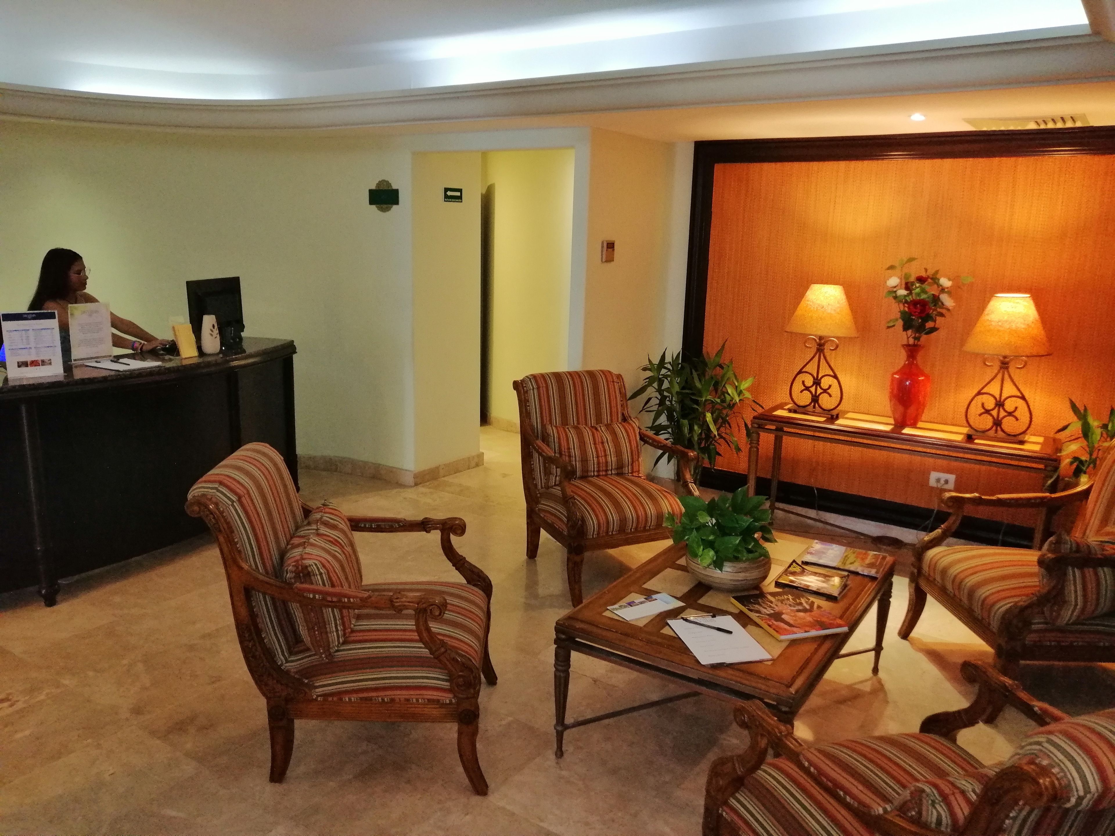 Um lobby com poltronas listradas, um balcão de recepção e uma área de atendimento com duas luminárias e um vaso de flores.