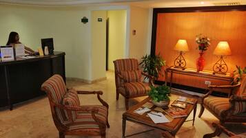 Um lobby com poltronas listradas, um balcão de recepção e uma área de atendimento com duas luminárias e um vaso de flores.