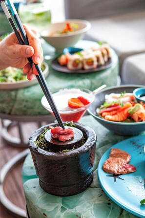 Et spisebord med forskellige retter, herunder sushi og en varm gryderet.