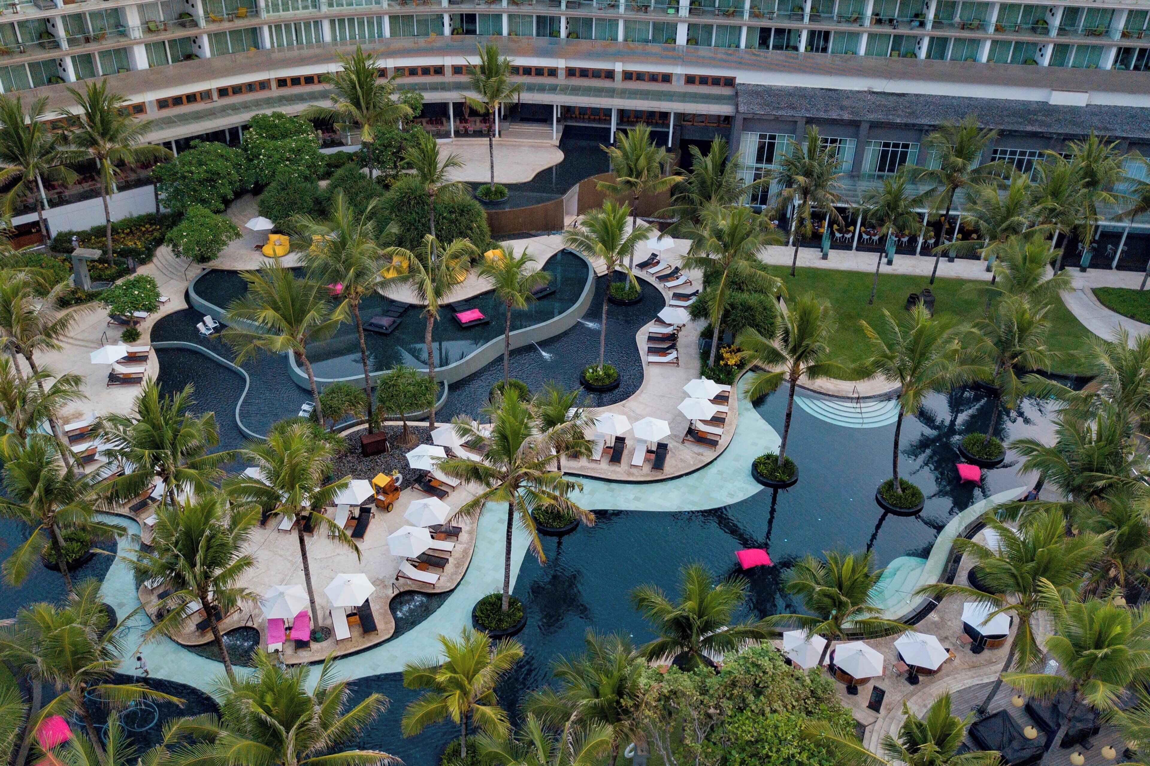 A resort with multiple swimming pools, palm trees, and lounge areas.