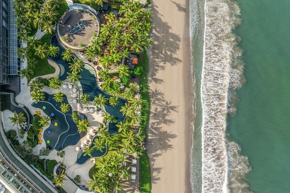 Oversigtsbillede af et resort med swimmingpool, palmer og en strand.