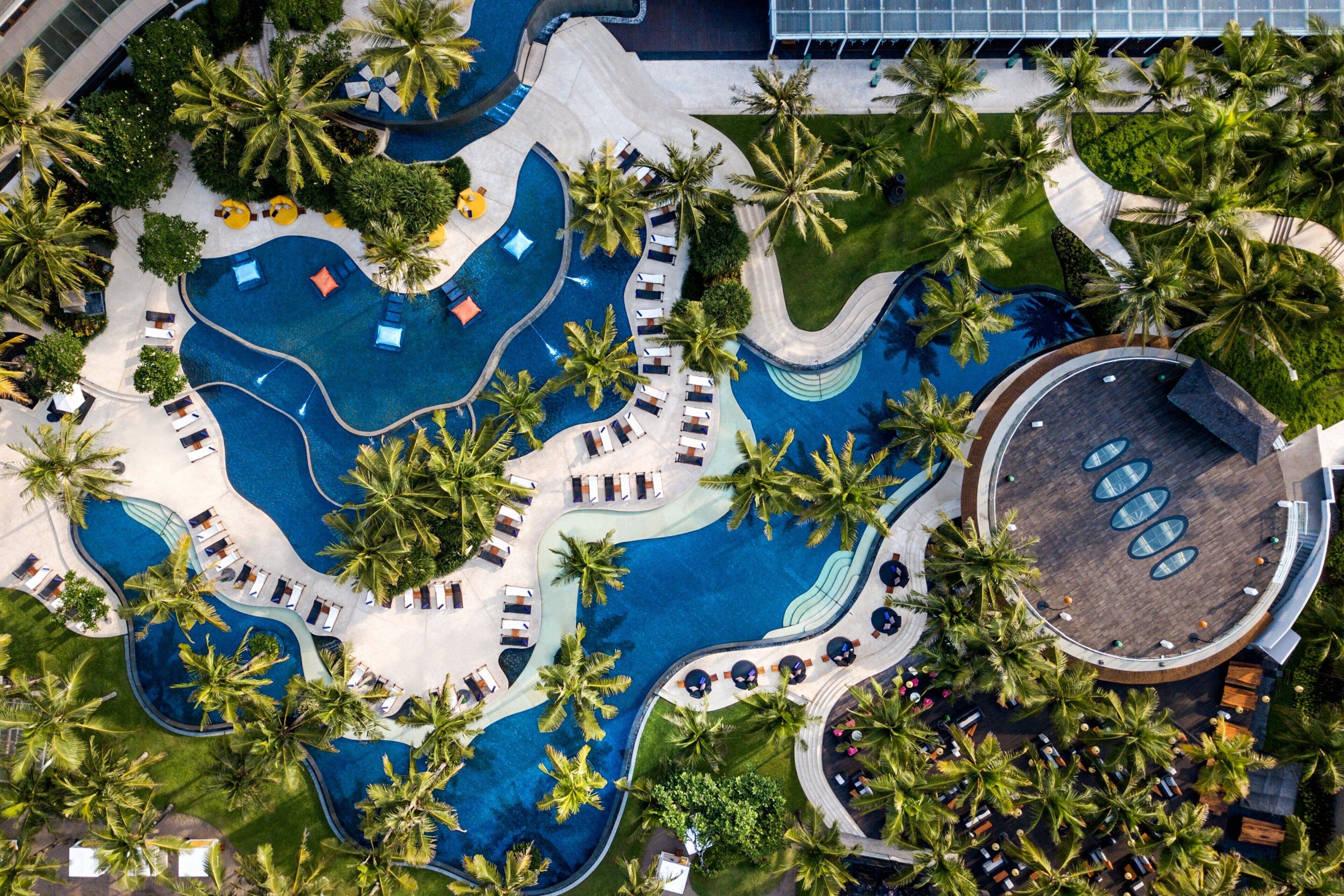 Vista aérea de um resort com várias piscinas, palmeiras e áreas de lazer.