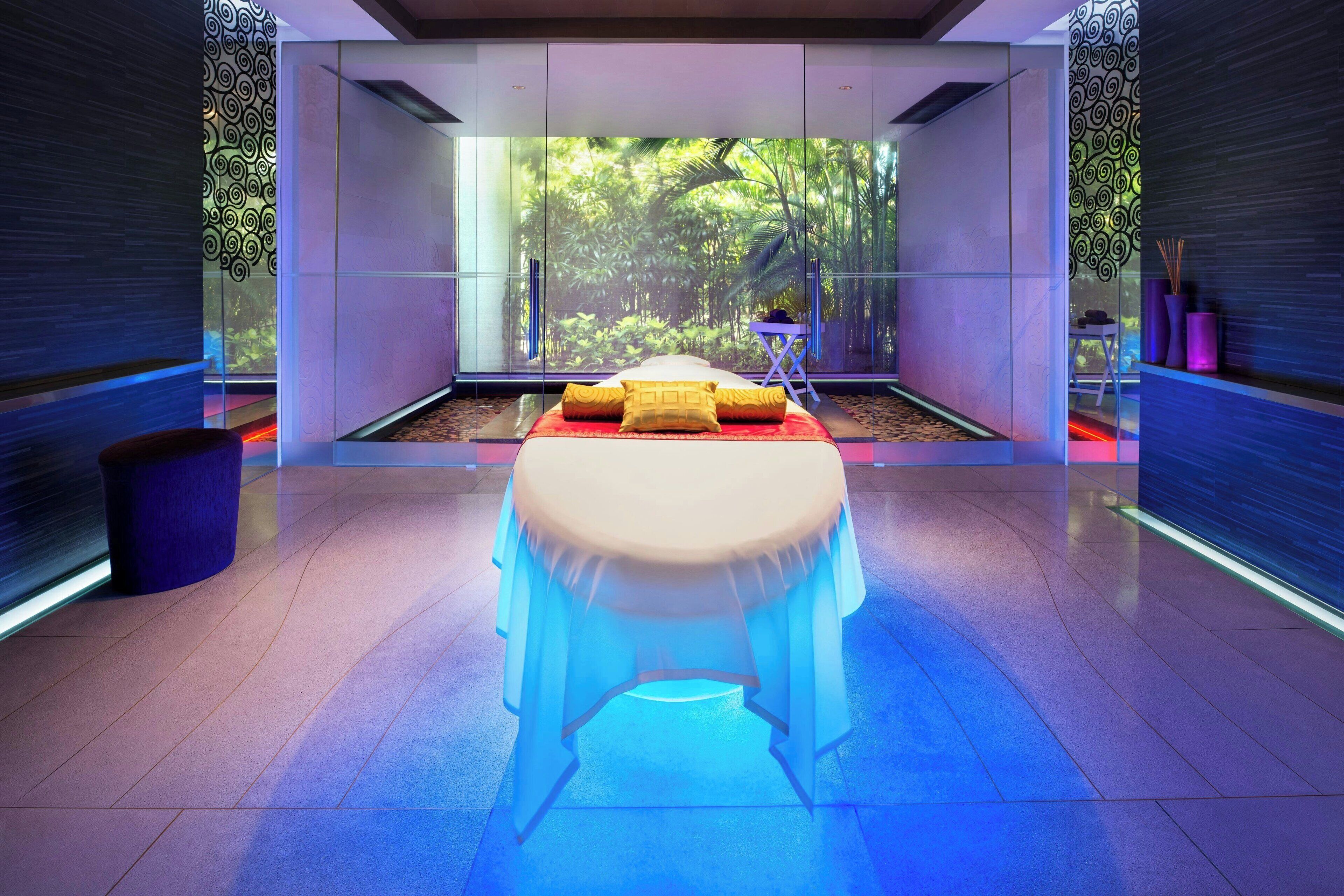 A modern spa room with a glass-enclosed massage table, a small side table, and a trash bin.