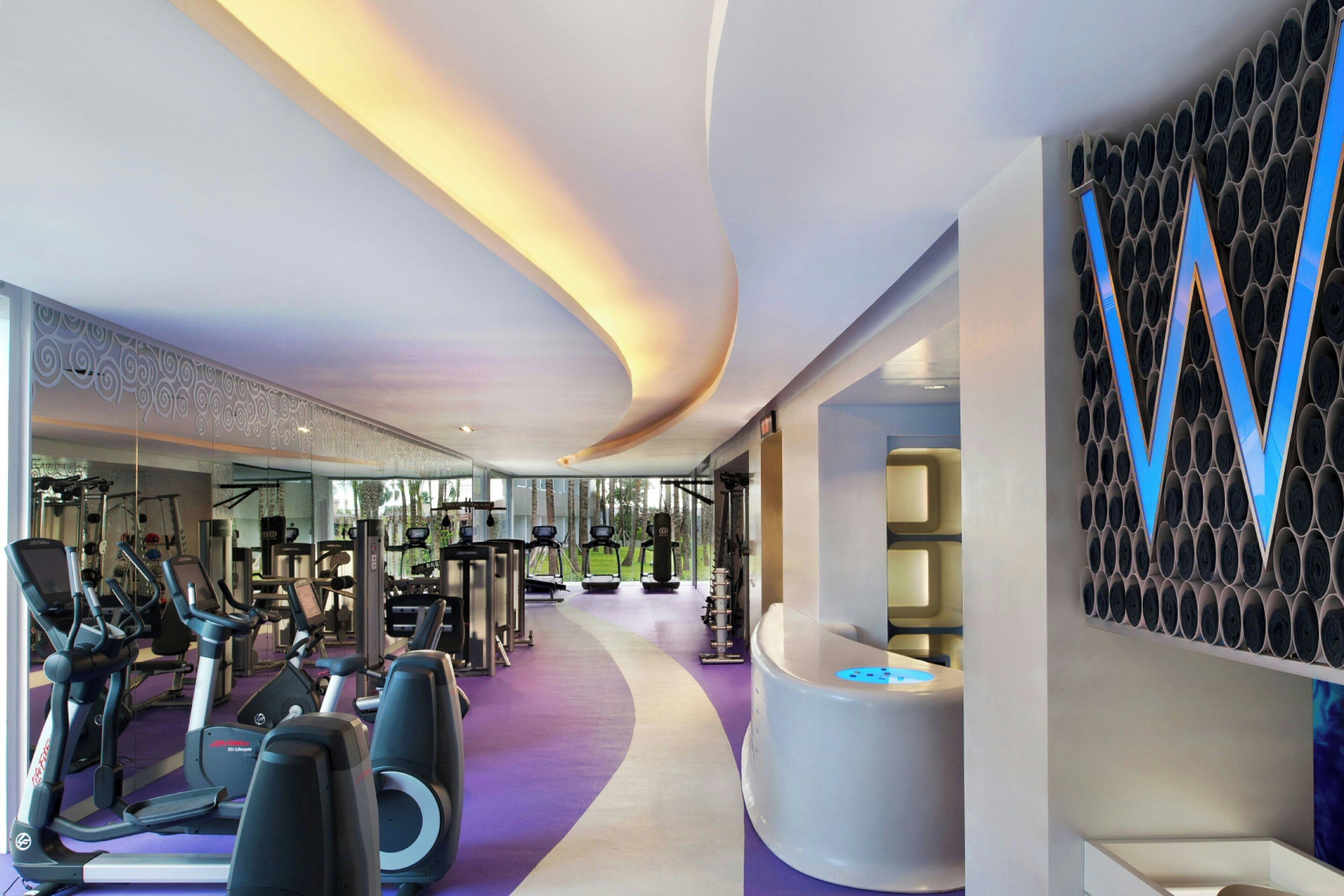 A modern gym with cardio machines, weight stations, and a large mirror.