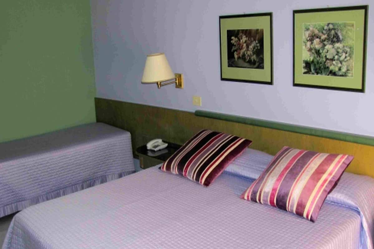 Een hotelkamer met twee eenpersoonsbedden, een nachtkastje met een lamp en twee ingelijste bloemstillevens aan de muur.