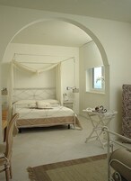 Un dormitorio con una cama con dosel, una mesita con tetera y una ventana con vista al cielo.