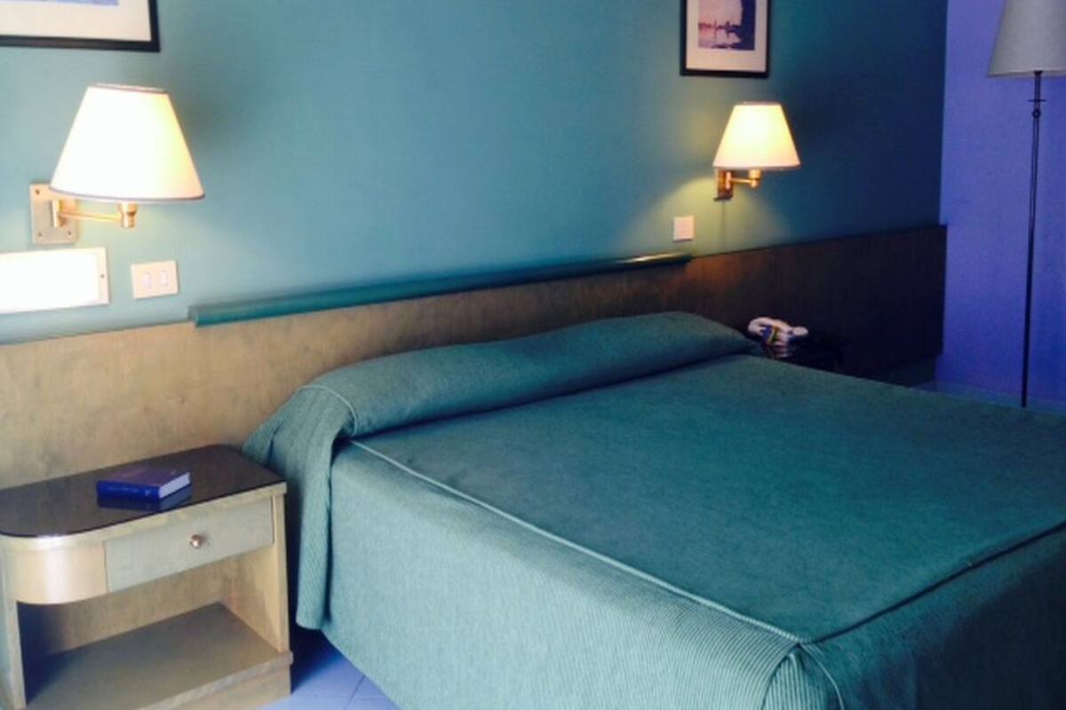 Een hotelkamer met een bed, een nachtkastje, twee wandlampen en een ingelijste foto aan de muur.