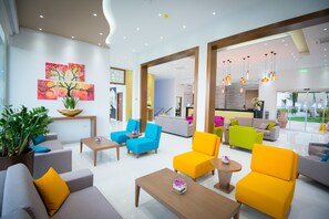 A modern hotel lobby with bright yellow and blue seating, a large potted plant, and artwork on the walls. - Loutsiana Hotel Apts (Ayia Napa)