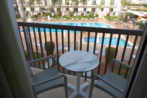 A balcony with a marble table and two chairs, overlooking a pool area with lounge chairs and umbrellas. - Loutsiana Hotel Apts (Ayia Napa)