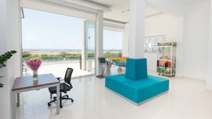 Um espaço de escritório moderno com uma janela grande, um sofá azul, uma mesa com um computador e uma unidade de exibição colorida.