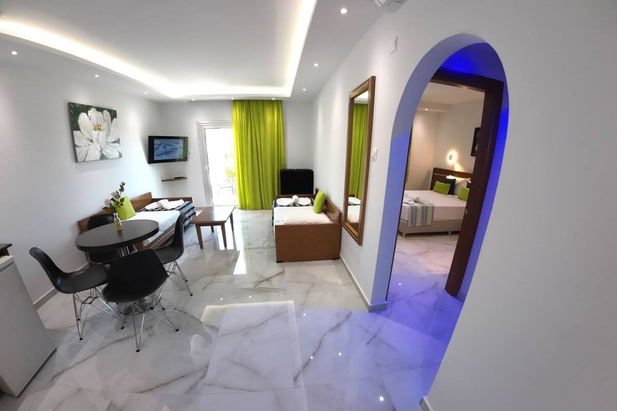 A modern hotel room with a dining area, a large mirror, and a view of the adjacent room.