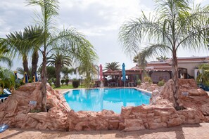 A pool surrounded by rocks and palm trees, with a sign indicating no diving. - Loutsiana Hotel Apts (Ayia Napa)