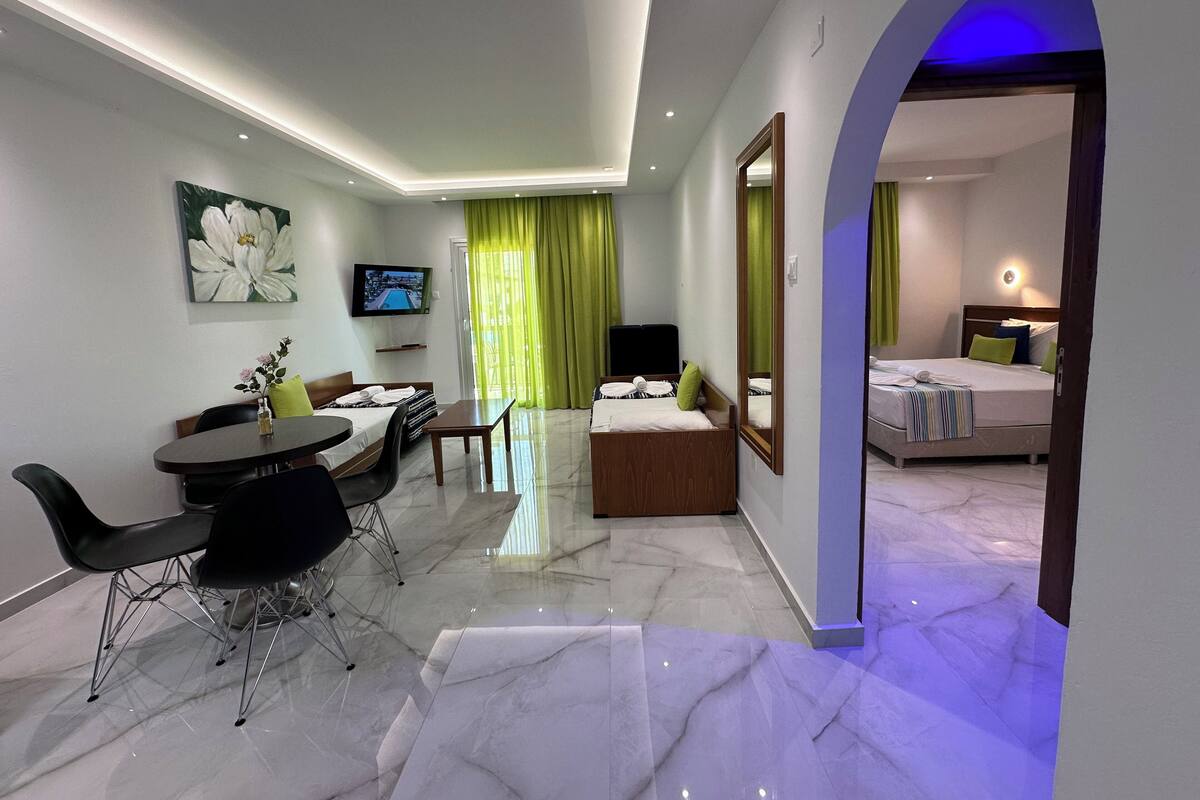 A hotel room with a dining area, a TV, a bed, and a bathroom visible through an archway.