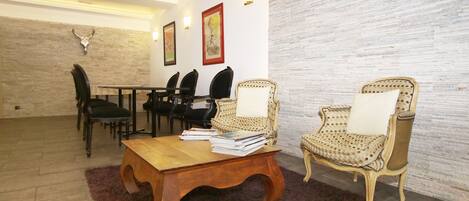 A room with a wooden coffee table, two wicker chairs with cushions, a dining table with chairs, and a stone wall with a mounted animal head.