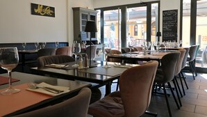 A restaurant interior with tables set for dining, a blackboard menu, and a view of the street outside. - Hotel Napoléon (La Turbie)