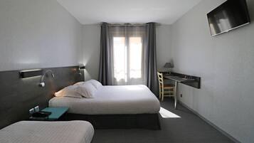 A hotel room with two beds, a desk, a TV, and a window with curtains.