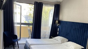 A hotel room with two beds, a chair, a TV, and a balcony with curtains. - Hotel Napoléon (La Turbie)