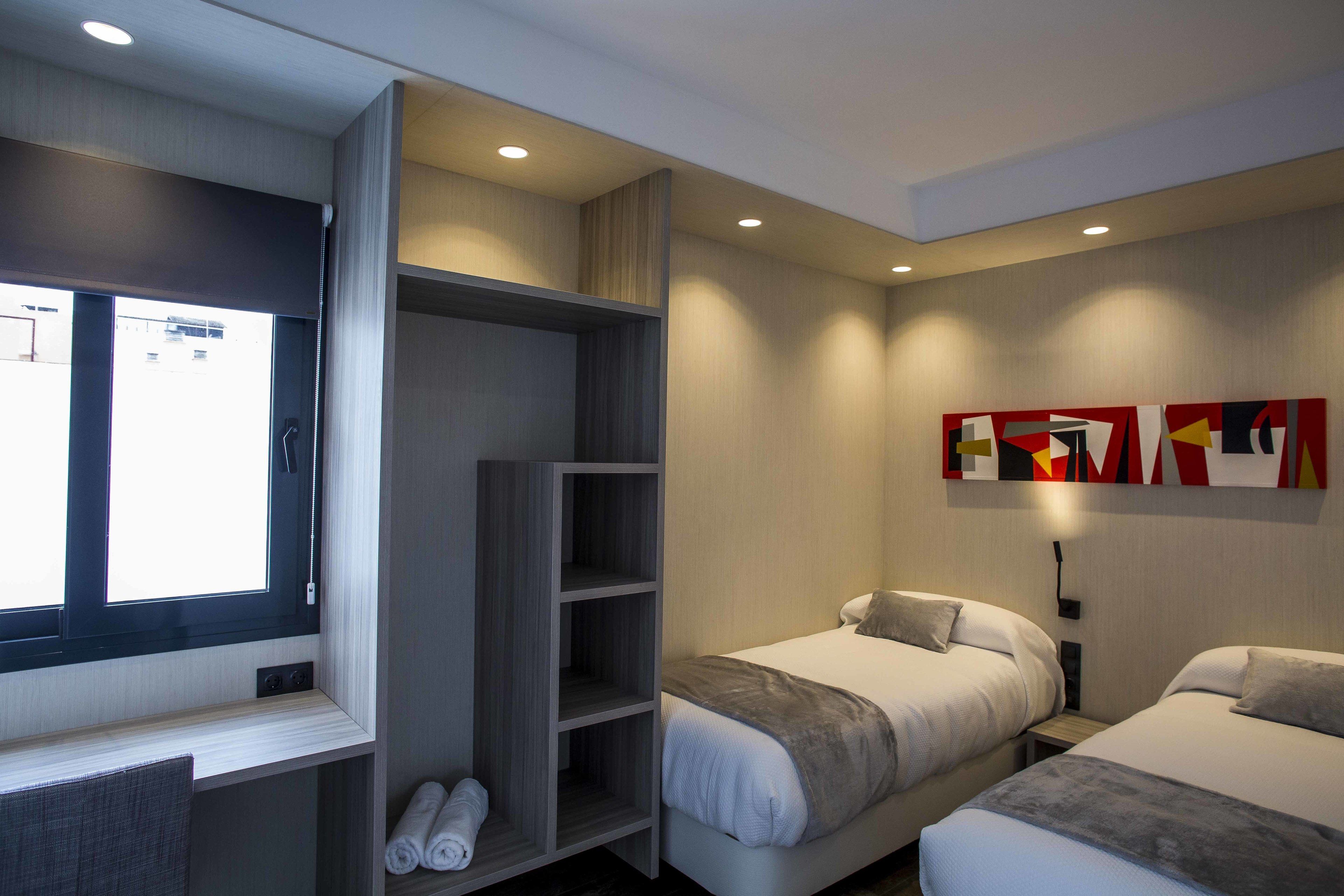 Een moderne hotelkamer met twee bedden, een grote kledingkast, een raam met zonwering en een kunstwerk aan de muur.