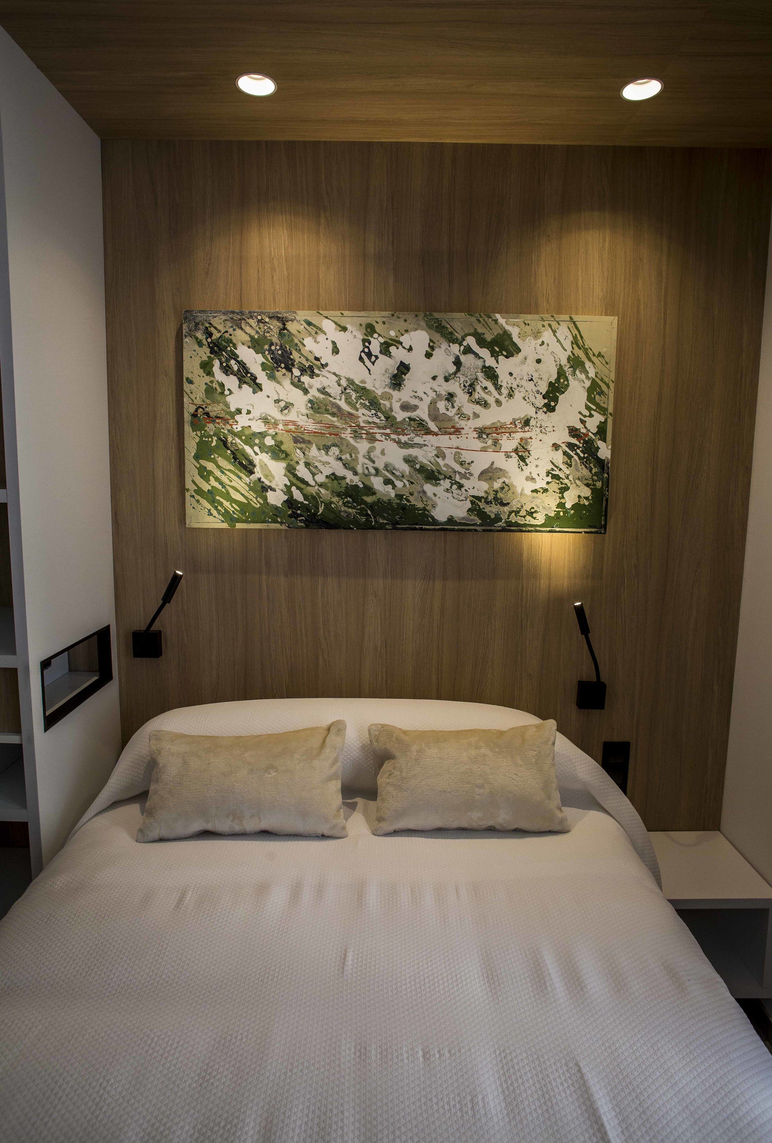 A bedroom with a large bed, two bedside tables, a wooden headboard, and a wall-mounted artwork.