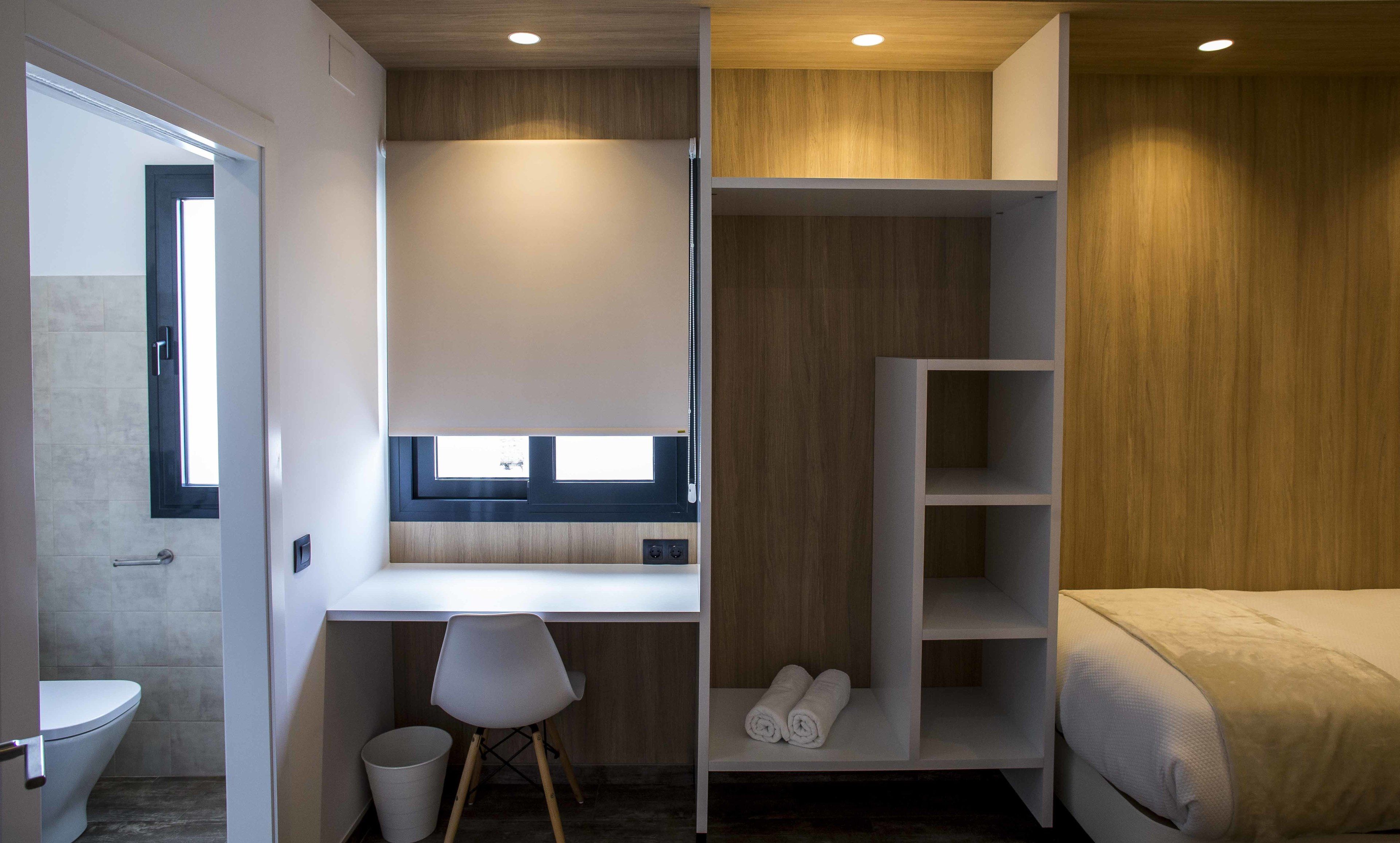 A modern room with a built-in desk, a shower, and a bed.