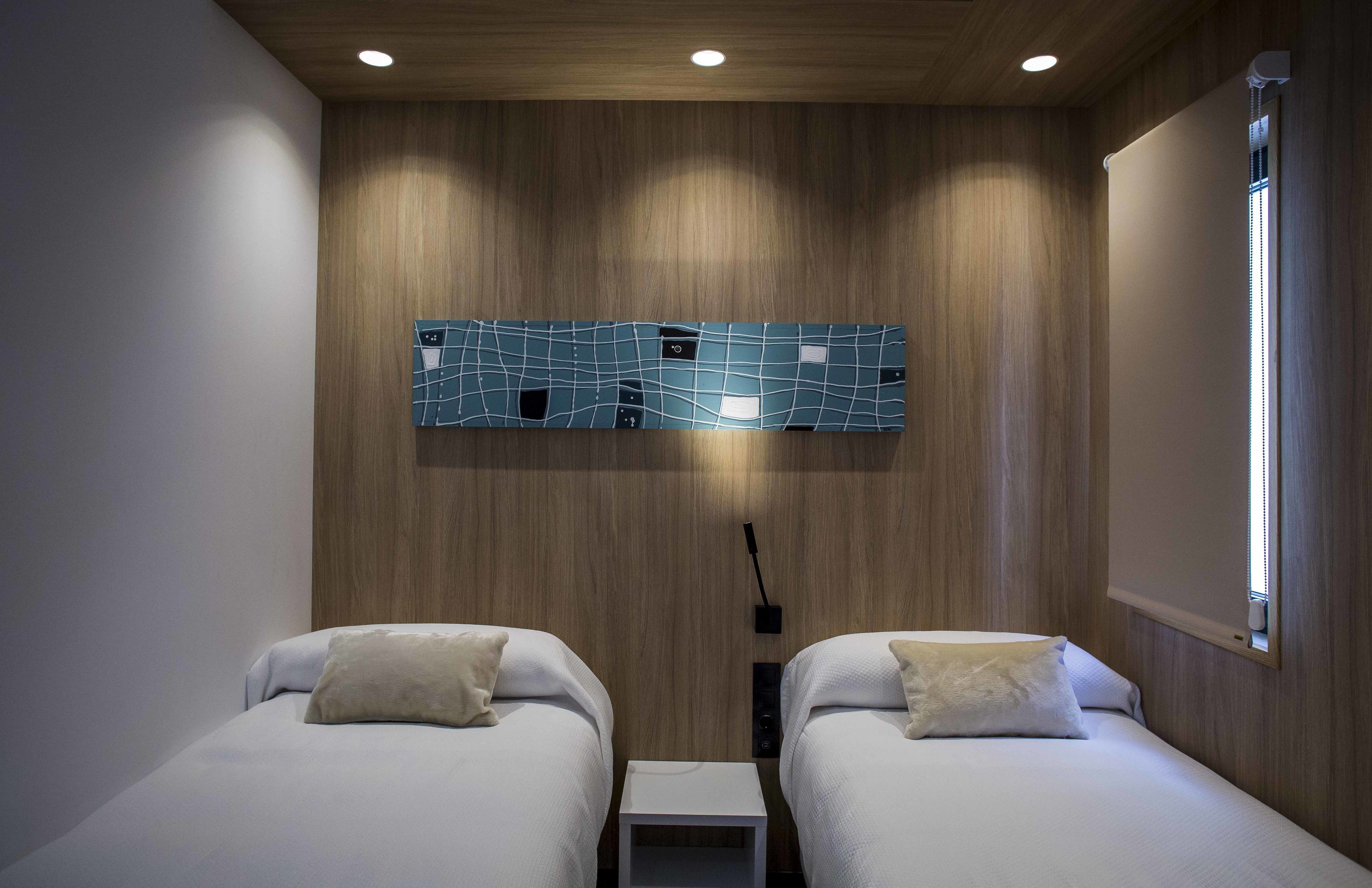 Quarto de hotel moderno com duas camas, painéis de parede de madeira, uma obra de arte original e uma janela com persianas.